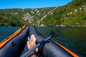 Kayaking on the lake with man legs in point of view with beautiful mountain landscape in the background.
