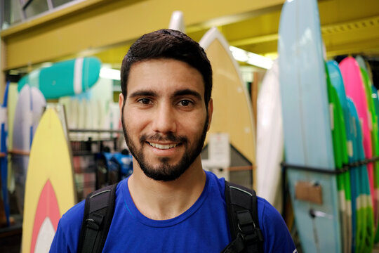 Positive portrait of adult male latin bearded surfer on surf board shop store buying with smile, happy, facing camera, colorful background indoors. - Powered by Adobe