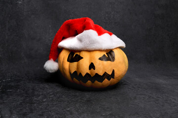 big orange ripe pumpkin with painted scary mystical face wearing santa claus hat, halloween and...