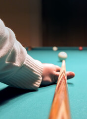 Game of billiards. A hand with a cue hits a billiard ball on the table. Vertical photo.