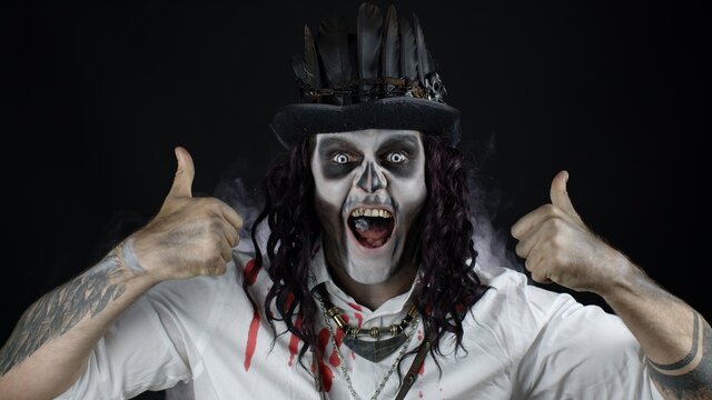 Frightening smiling man in skeleton Halloween costume showing thumbs up gesture. Black background