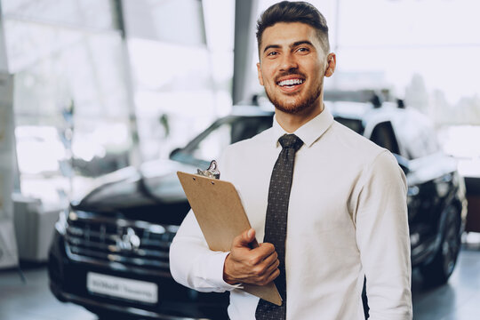 Friendly handsome car seller man standing in car salon