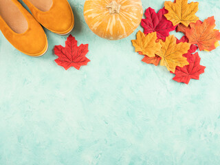 Female trendy yellow mustard flat shoes with autumn leaves and pumpkin, seasonal symbols over turquoise background. Flat lay, copy space