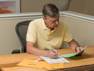 Senior caucasian man seated at home desk and completing the mail-in or absentee ballot for the 2020...