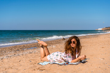 Fototapeta na wymiar Young woman in sunglasses and dress lying on the beach in front of the sea