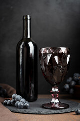 Carved retro style purple wineglass full of cabernet red wine and bottle with ripe isabella grape...