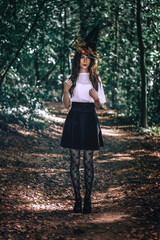 Young pretty witch in black hat close up in the forest. Whitch halloween cosplay. Art processing.