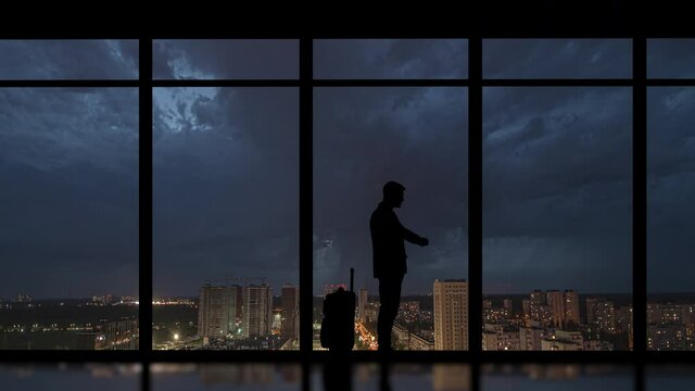 The man with suitcase stands indoors on the rainy city background. time lapse