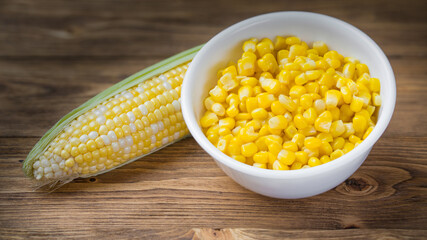 Bowl with corn seeds and ripe corn cobs on wooden table. Raw and tinned corn.