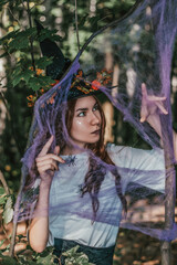 Young pretty witch in black hat close up in the forest. Whitch halloween cosplay. Art processing.