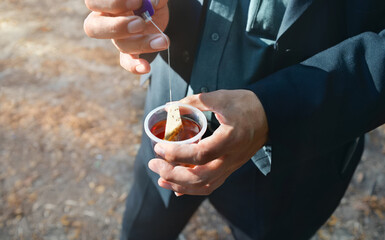 Man’s hands holding plastic cup with tea bag. Eating in a hurry on the move. Plastic tableware.