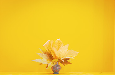 close up image of many autumn leafs in a stylish vase on the shelf with yellow blank space background