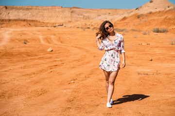 A young woman with long hair in a short dress walks through the orange rocky desert on a hot day