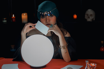 Mysterious beautiful woman fortune teller with crystal ball, holding tarot card