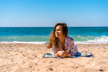 Young woman in sunglasses and dress lying on the beach in front of the sea