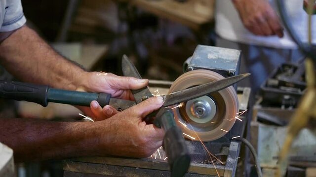Machine sharpening of fence shears, sharpening of fence shears on electric grinder, hand sharpens scissors on rotary grinding stone, close-up