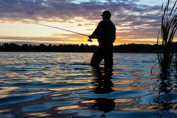 Silhouette of angler catching the fish durring sunset 