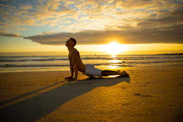 Man practicing yoga on the beach during sunrise/sunset
