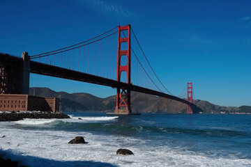 Fototapeta na wymiar Golden Gate Bridge, San Francisco, California USA. Classic panoramic view, famous landmark. Touristic attraction, travel destination at sunny surf beach day, of blue clear sky. Surfing next Fort Point