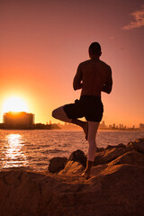 Man practicing yoga on the beach during sunrise/sunset