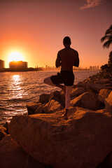 Man practicing yoga on the beach during sunrise/sunset