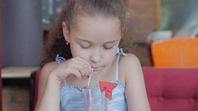 Cute baby girl drinking a glass of watermalon in a cafe. little girl drinking water. Close-up. The child is drinking a cup of juse.