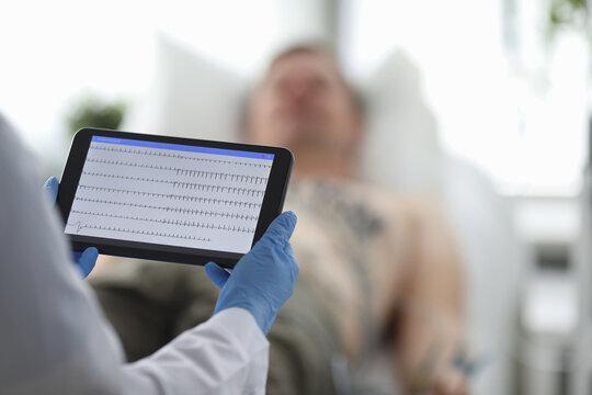 Doctor with ecg monitor stands in front of patient in background. Diagnosis of diseases of cardiovascular system concept.