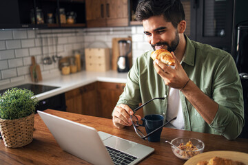 Portrait of man eating breakfast and looking at laptop