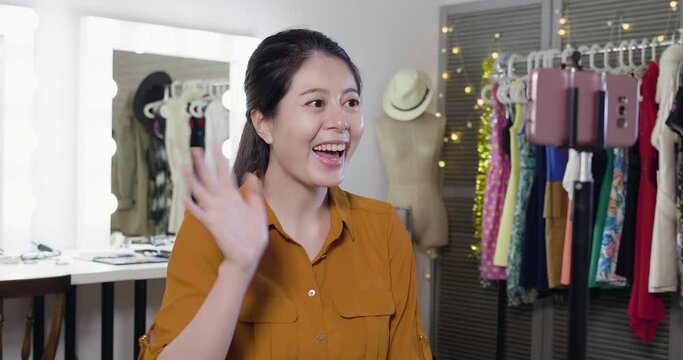 slow motion of asian girl blogger in backstage makeup place before going on stage. young woman recording video on smart phone. smiling beauty wave hands and chatting with fans on live streaming.