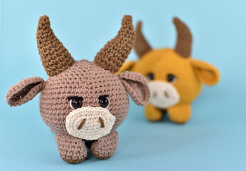Two bulls knitted from thick cotton yarn. They are placed on a blue background and standing one after another. One in focus, the other is deliberately blurred.