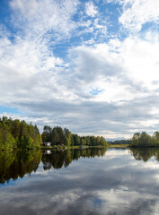 Fototapeta na wymiar Beautiful landscape in Finland at the lake shore. Reflecting waters and cloudy sky. Calm scenery for poster and wallpaper use.