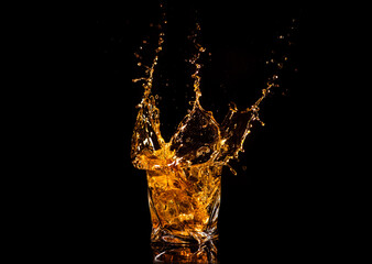 A glass of whiskey with splashes from the ice cube over black background. alcohol splashes. whisky or cognac or another type of alcohol ю