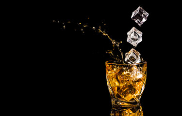 A glass of whiskey with splashes from the ice cube over black background. alcohol splashes. whisky...