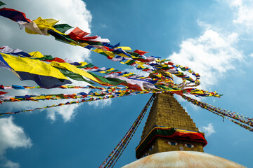 Multicolored Buddhist prayer flags with mantras on a background of blue sky and an ancient stupa. Traditional Tibetan and Nepalese threads with rectangular colored pieces of fabric.