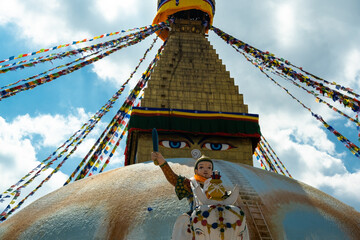 The upper part of the Boudhanath stupa in Kathmandu, Nepal. The image of Buddhas eyes on a gold surface of the stupa. Colorful prayer flags nearby. Buddha statue on a white elephant.