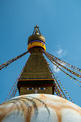 The upper part of the Boudhanath stupa in Kathmandu, Nepal. The image of Buddhas eyes on a gold surface of the stupa. Colorful prayer flags nearby.