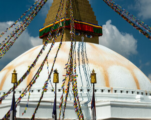 The upper part of the Boudhanath stupa in Kathmandu, Nepal. The image of Buddhas eyes on a gold surface of the stupa. Colorful prayer flags nearby