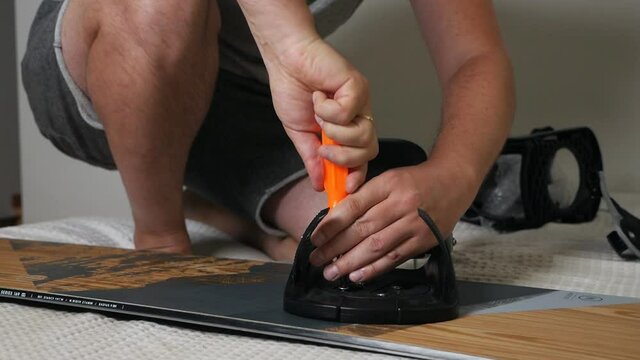 The man's hand attaches the bindings to the snowboard. Prepares the snowboard for winter