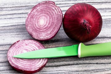  a whole red onion ands a cut red onion on a dark cutting board with a vegetable knife