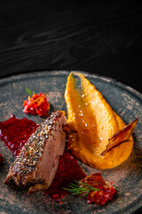 Roasted Duck breast fillets with pumpkin pure in plate on black wooden table background