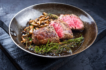 Gebratenes dry aged Angus Filet Steak natur vom Rind Kräuterseitlinge Pilze und Kräuter angeboten als Draufsicht in einer rustikalen Bratpfanne