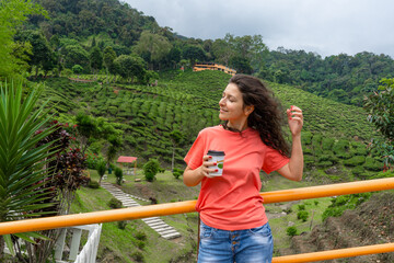 Brunette tourist girl enjoys tea from a craft cup against the background of a green tea valley.