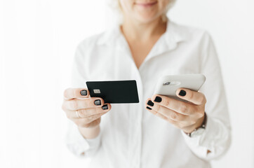 Unrecognizable woman holding black credit card and smartphone, making online payment, online shopping