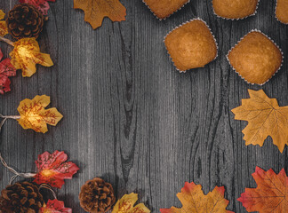 
muffins and autumn leaves

muffins, fall leaves, pine cones and garland on a black wooden table with a place for text in the middle, top view close-up.