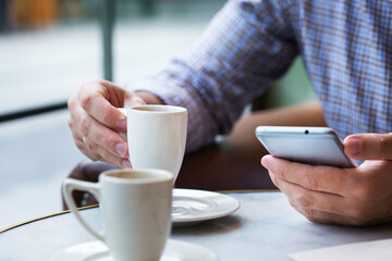 Businessman sitting in cafe, drinking morning coffee and using smartphone
