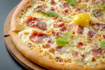 Pizza carbonara. Contains egg yolk, cream, bacon, parmesan. Served on a black background.