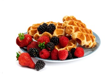 a pile of Belgian waffles with strawberries raspberries and blackberries on a blue plate isolated on white