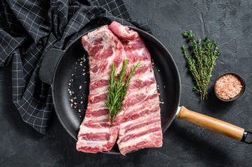 Raw pork spare ribs with spices and herbs in a pan. Black background. Top view