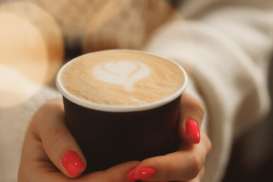 Female hands in sweater holding a cup of latte coffee