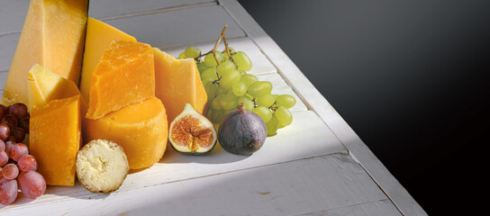 various varieties of hard cheese with grapes and figs on a white table in a sunbeam with a place...